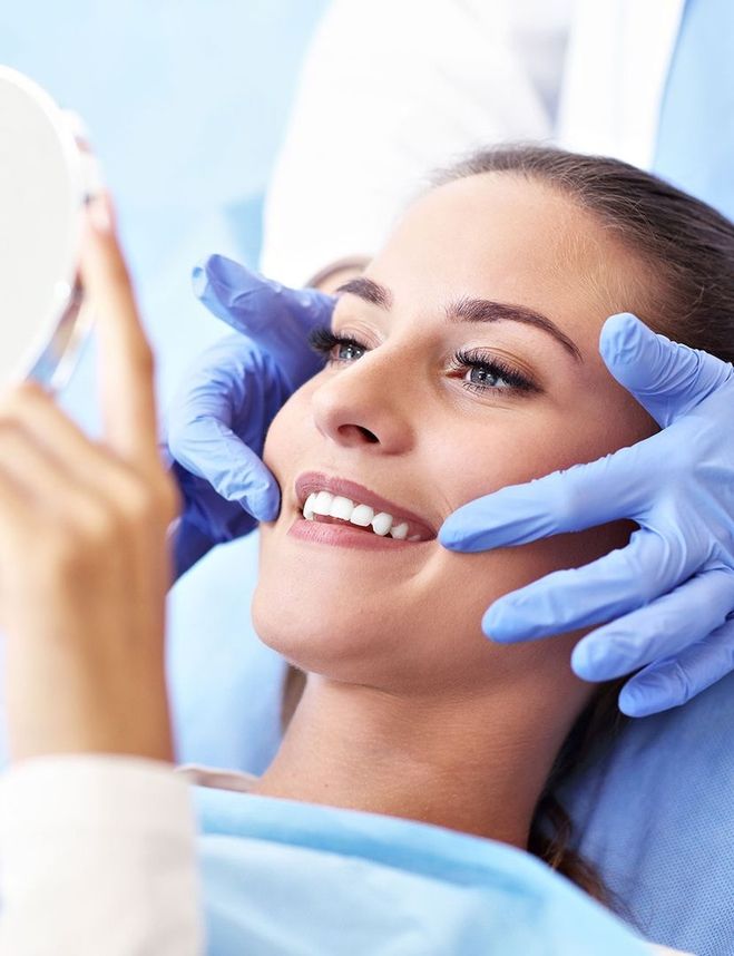 Patientin betrachtet ihr Lächeln nach der Zahnbehandlung im Handspiegel