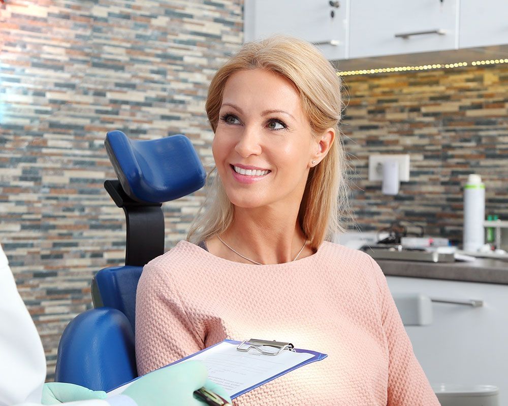 Frau im Behandlungszimmer lächelt zufrieden nach einem Zahnarzttermin