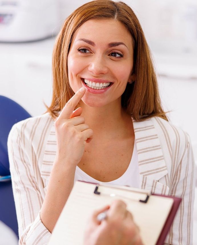 Patientin lächelt beim Beratungsgespräch in der Zahnarztpraxis und zeigt auf ihre Zähne