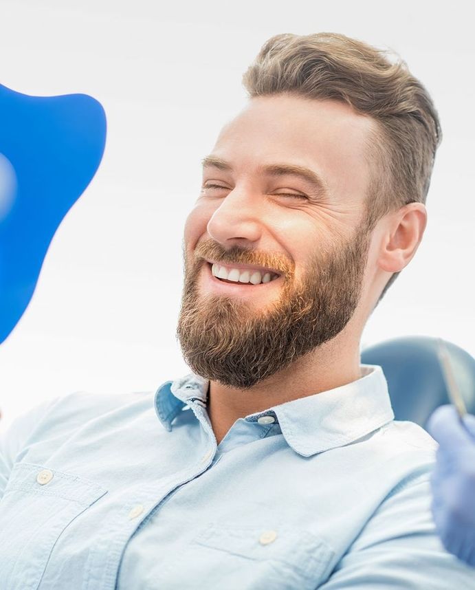 Mann mit Bart freut sich nach erfolgreicher Zahnbehandlung und betrachtet sein Lächeln im Spiegel